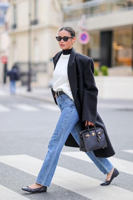 Modella con jeans, maglioncino bianco, cappotto e borsa neri e occhiali da sole