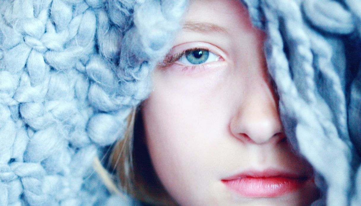primo piano ragazza pelle chiarissima occhi azzurro chiaro e coperta di lana in testa