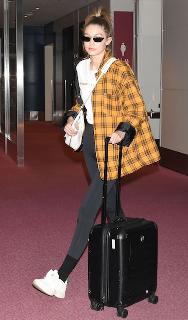 Gigi Hadid con leggins neri, valigia e camicia a quadri gialli