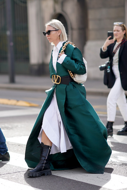 Modella con abito bianco, cappotto verde petrolio, stivali neri e borsa bianca