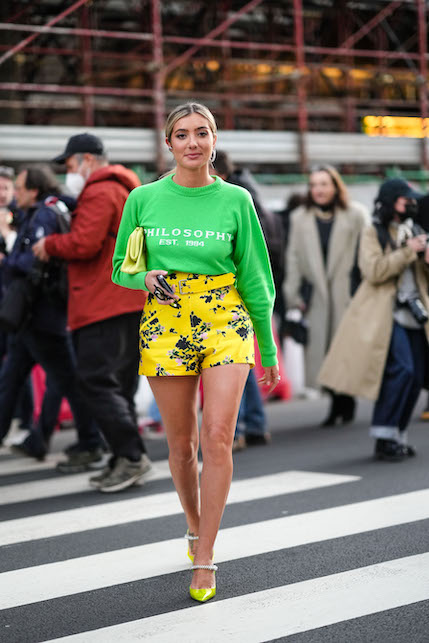 Modella con felpa verde, pantaloncini gialli in fantasia, scarpe e borsa gialle