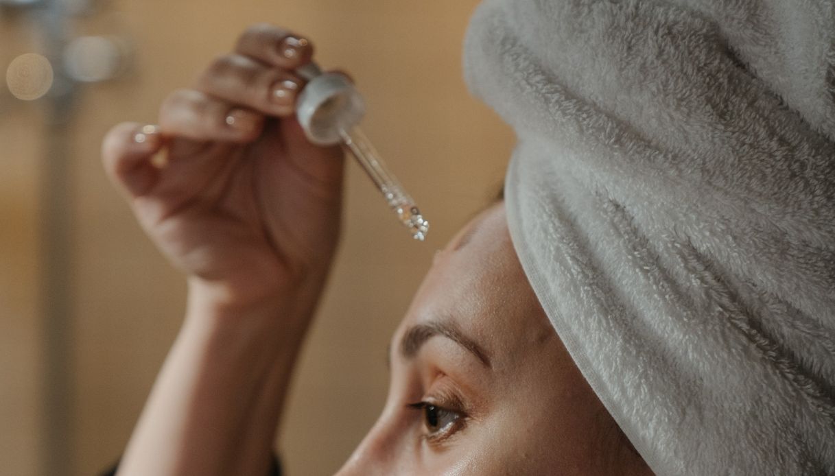 volto di donna con turbante bianco che applica il siero sul viso da una pipetta di vetro