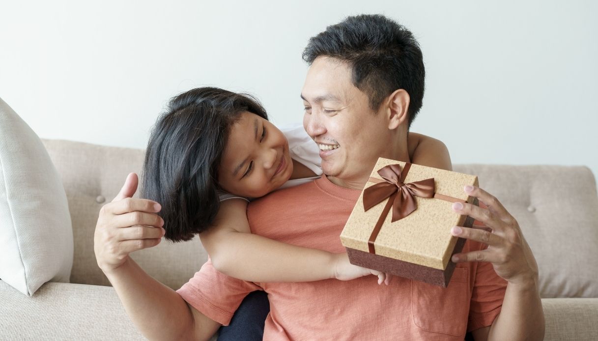 bambina asiatica abbraccia al collo il padre e gli dà un regalo
