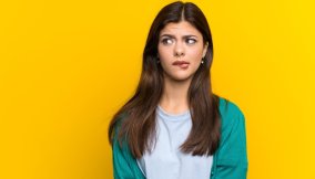 Teenager girl over yellow wall having doubts and with confuse face expression