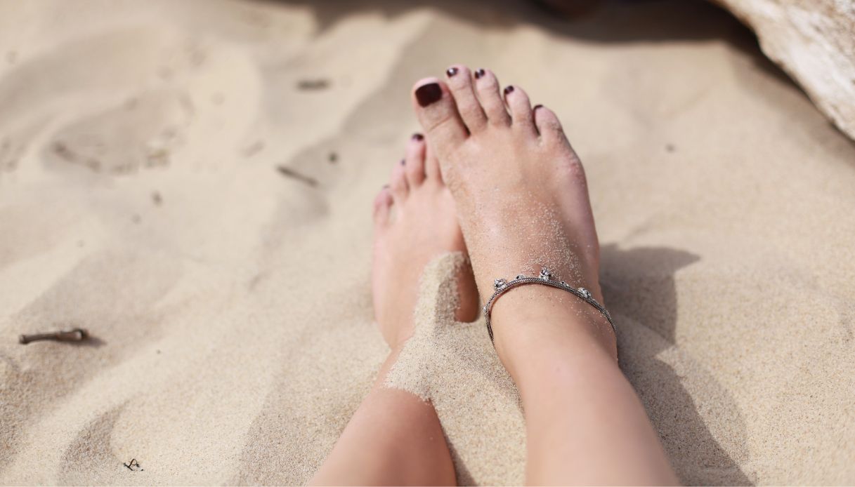 piedi donna con smalto bordeaux e cavigliera sulla sabbia