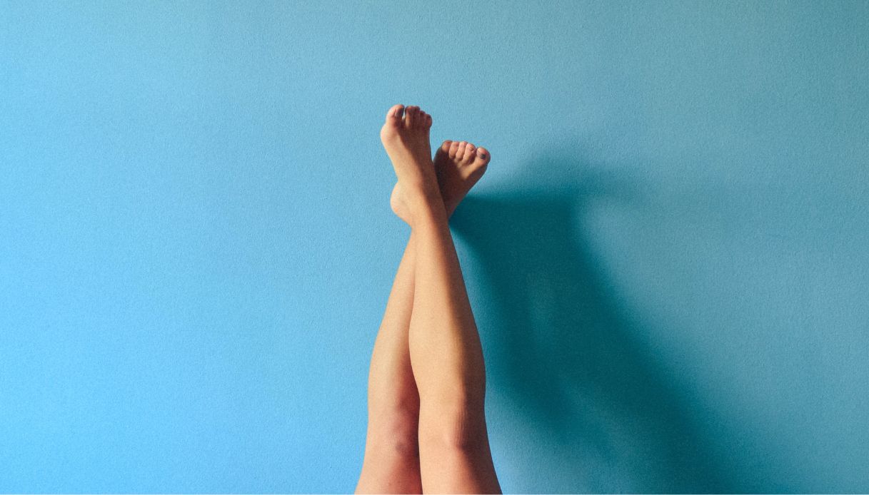 sfondo azzurro gambe incrociate contro il muro e piedi smalto nero