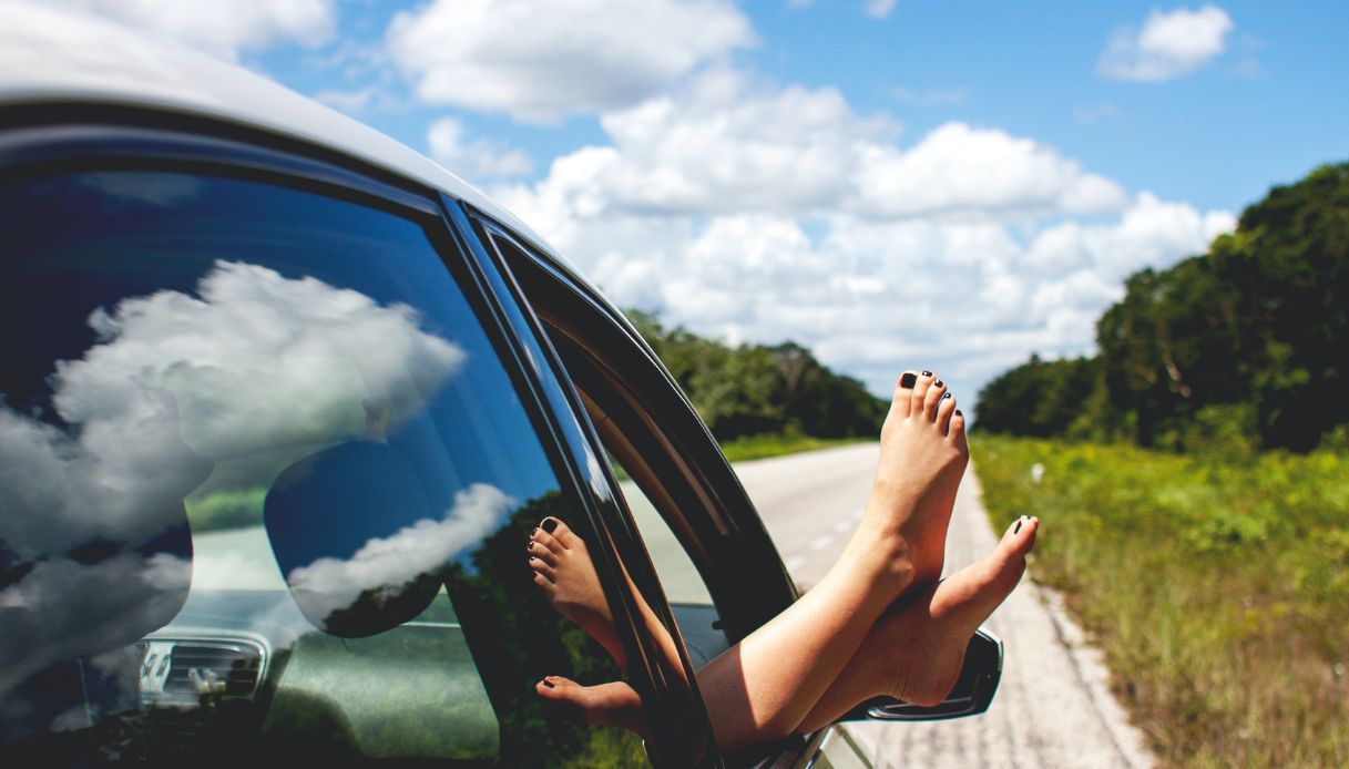 piedi con smalto nero fuori dal finestrino della macchina con sfondo di cielo con nuvole
