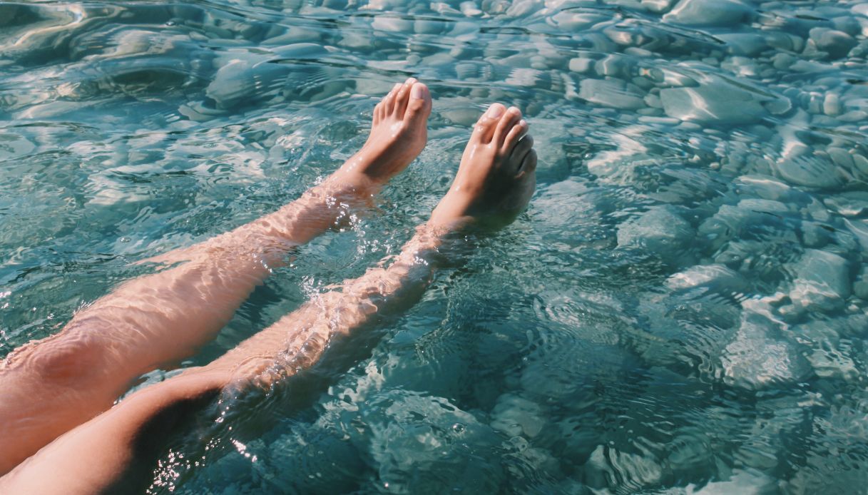 gambe femminili dentro acqua cristallina con riflessi del sole