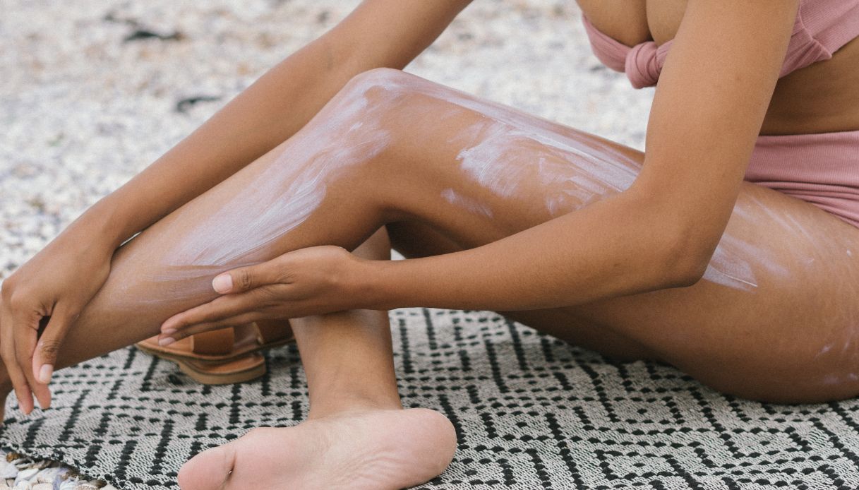 donna pelle scura applica crema su gambe al mare