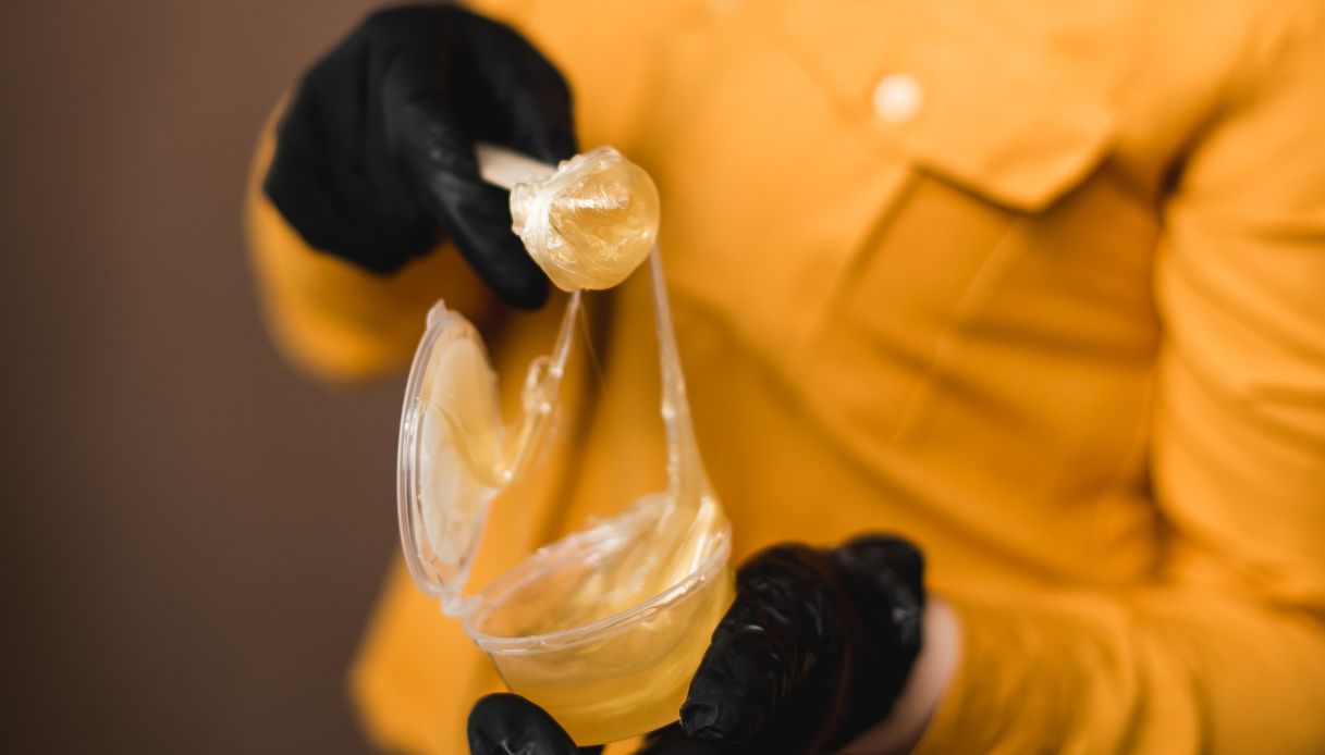 ceretta brasiliana maneggiata da estetista con guanti neri e camice giallo