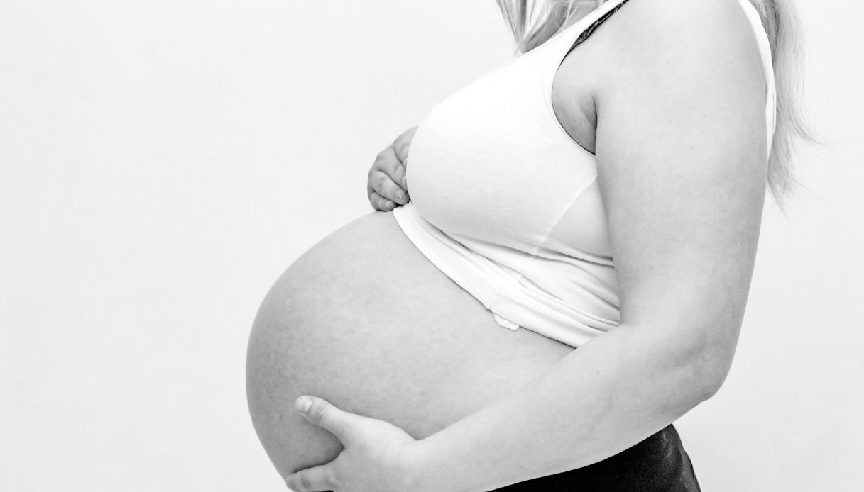 primo piano in bianco e nero di donna incinta che si tocca la pancia con canottiera bianca e capelli chiari