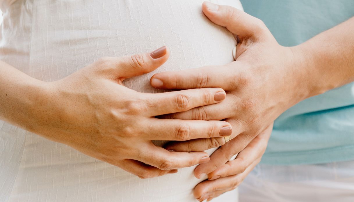 donna incinta porta mani sulla pancia incrociandole su vestito bianco