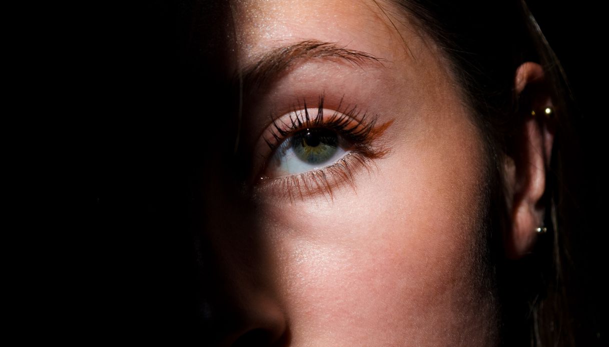 closeup occhio azzurro con eyeliner rosso e metà viso in ombra