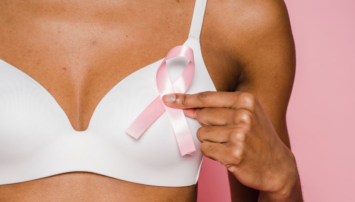 donna pelle scura con reggiseno bianco tiene fiocchetto rosa davanti al seno