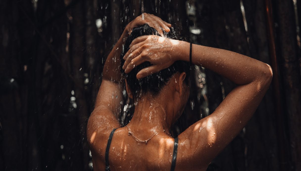 donna abbronzata di schiena che si lava i capelli sotto la doccia