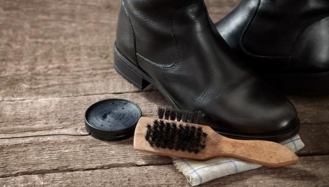 Spazzola per scarpe, olio di visone e un paio di stivali in pelle su  pavimento in legno