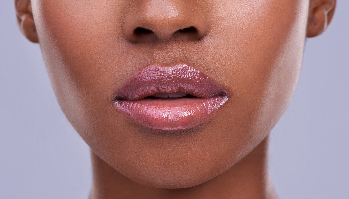 Primissimo piano sul volto di una donna nera che mostra al centro le sue labbra truccate con un lucidalabbra rosato