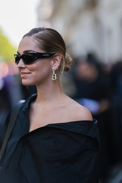 Chiara Ferragni con uno chignon basso e riga laterale mentre indossa occhiali da sole e una camicia nera aperta sulle spalle