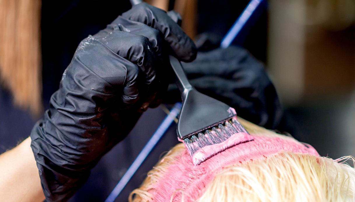 Un parrucchiere intento a colorare di rosa una chioma corta completamente decolorata
