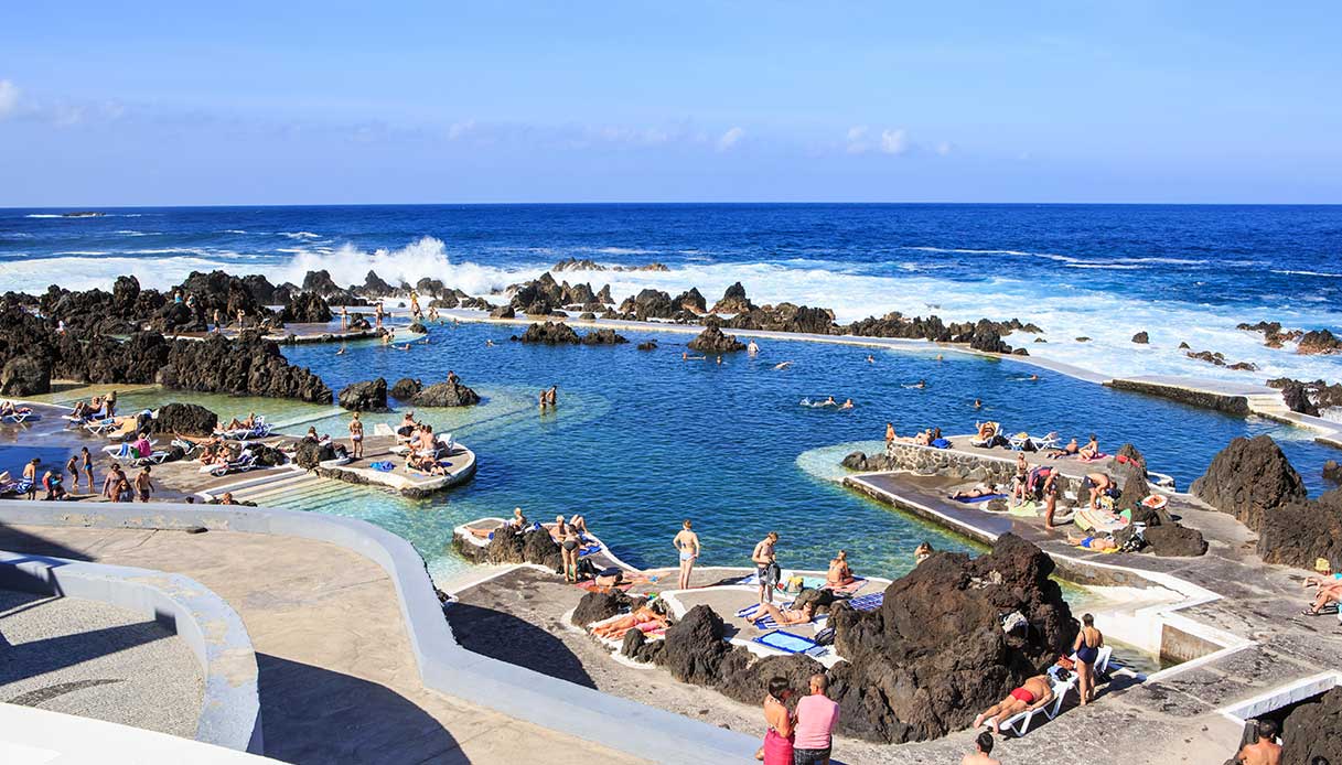 Vasche naturali create dalla lava, frequentate da bagnanti, con onde oceaniche sullo sfondo