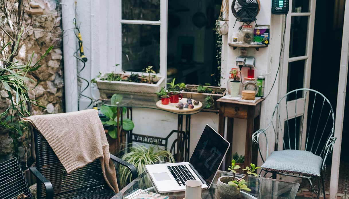 Spazio esterno con tavolo, computer e piante decorative.