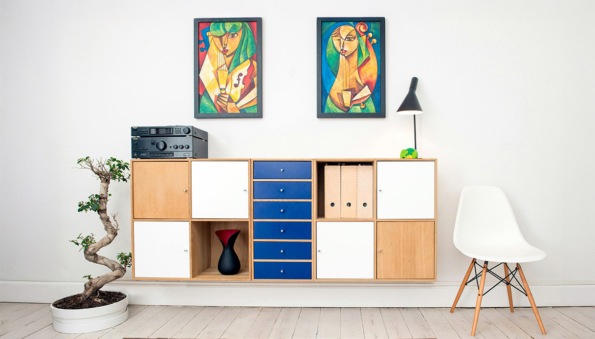 Mobile contenitore con ante bianche e cassetti blu sotto quadri colorati.