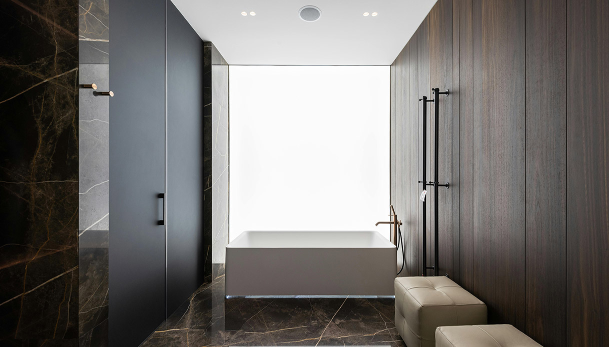 Bagno moderno con vasca rettangolare minimal, rivestimenti in pietra e legno scuro, stile essenziale e materico