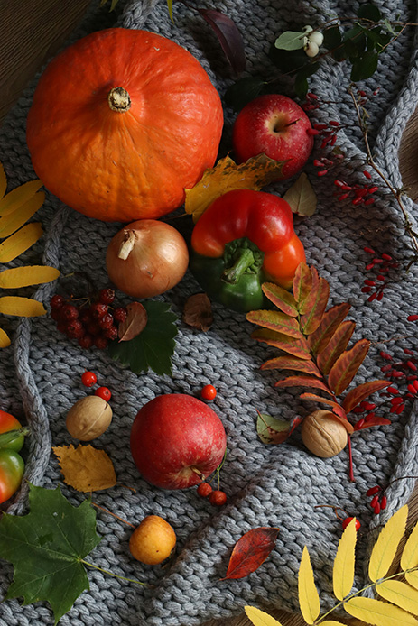 Zucca arancione, peperoni, mele, noci e foglie autunnali su una base di tessuto grigio intrecciato.