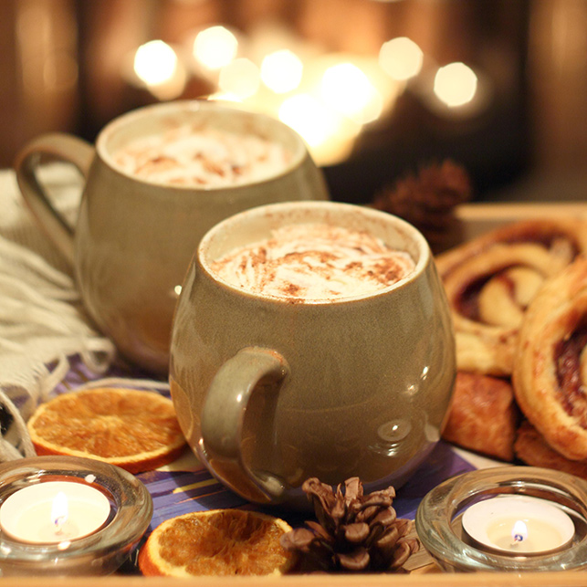 Due tazze di cioccolata calda con candele e dolci accanto al camino, atmosfera Hygge danese.