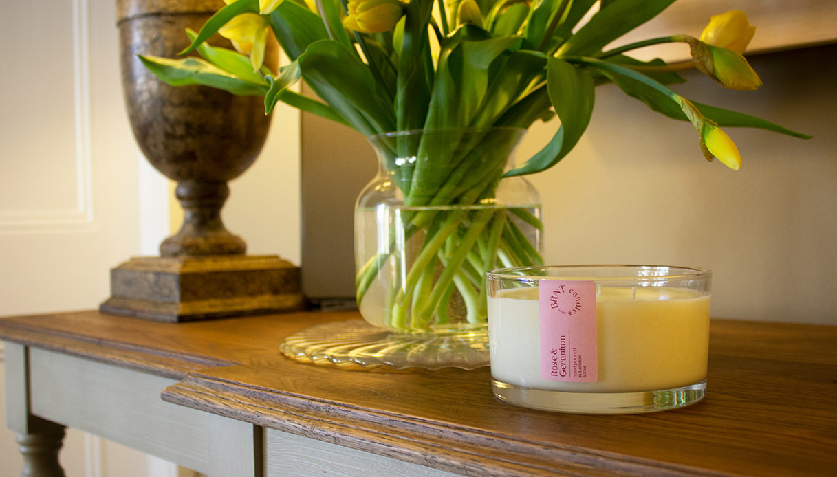 Candela gialla profumata accesa accanto a un vaso di tulipani su tavolo in legno