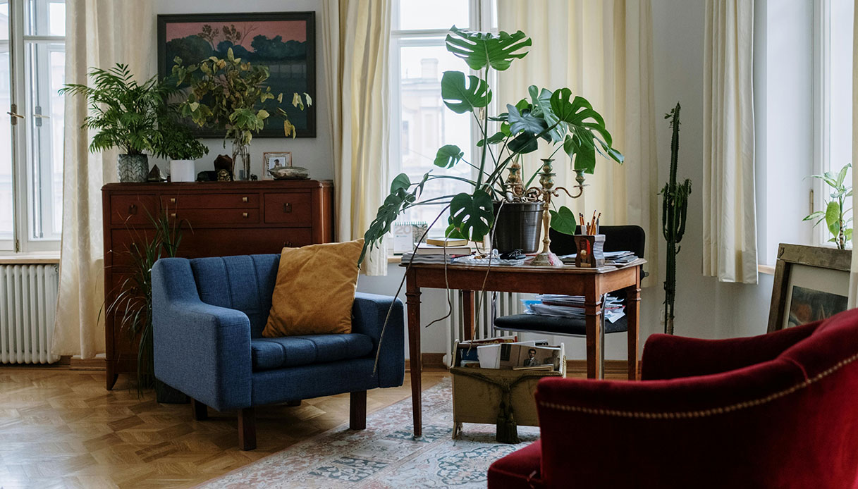 Salotto luminoso con poltrona blu e rossa, piante verdi e arredi in legno