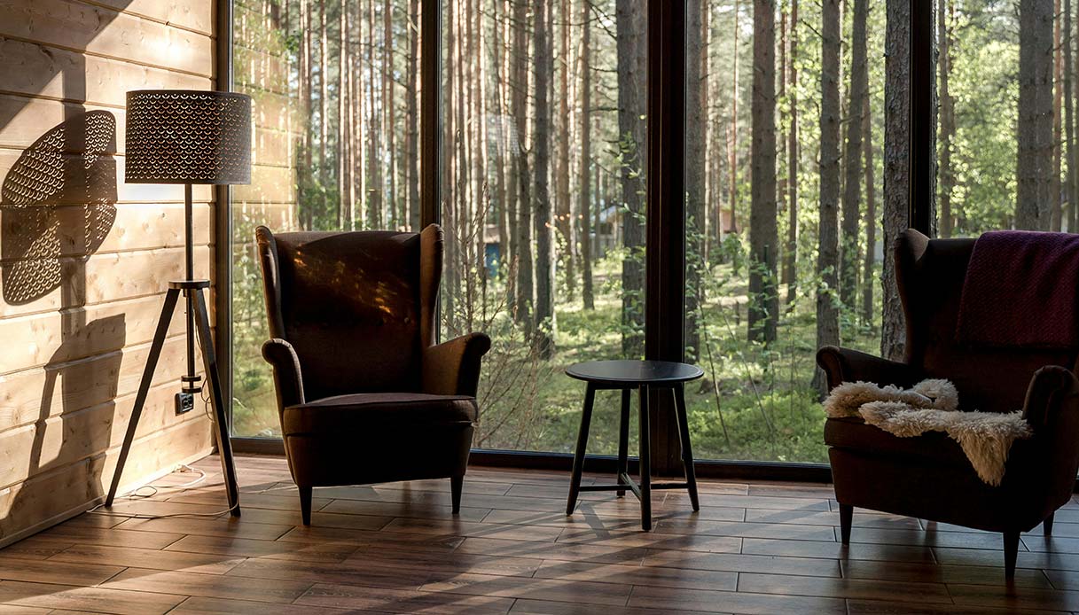 Due poltrone davanti a grande vetrata con vista su bosco in salotto rustico