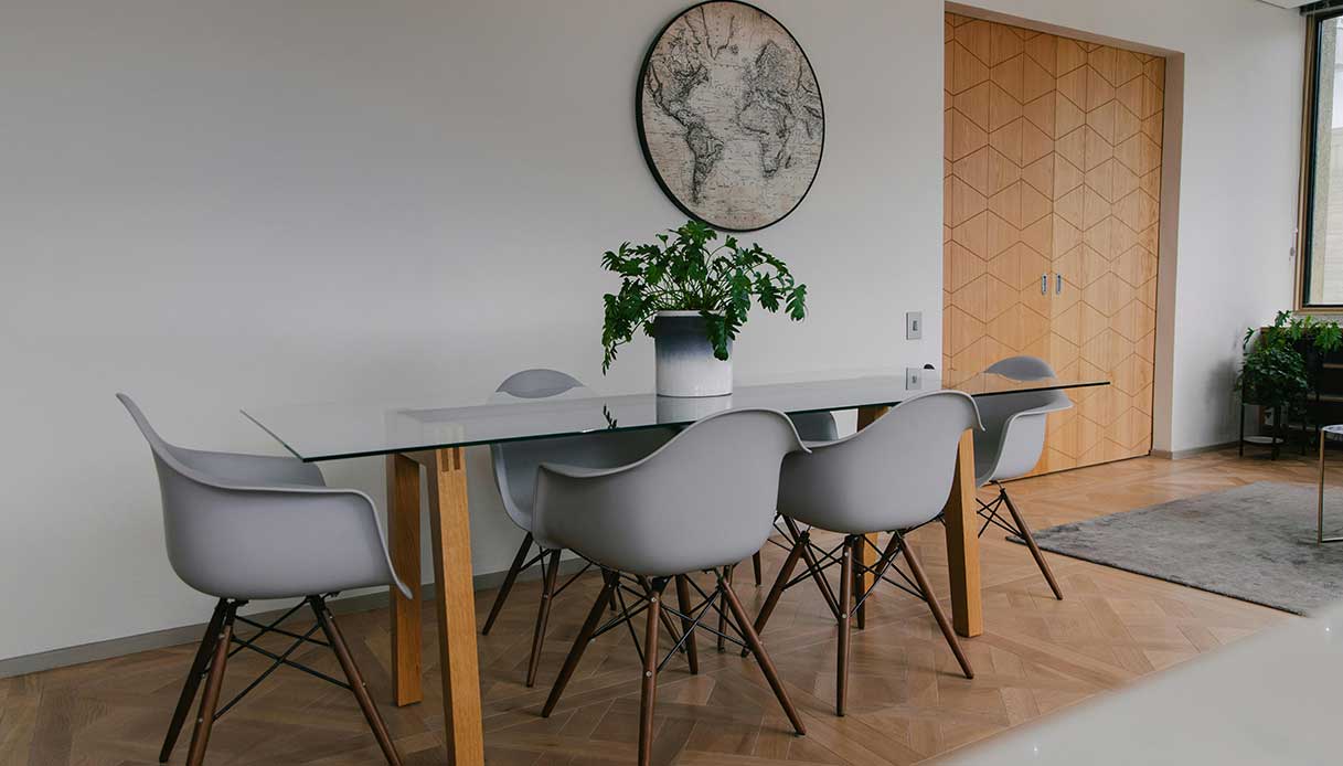 Sala da pranzo moderna con tavolo in vetro, sedie grigie e decorazioni essenziali