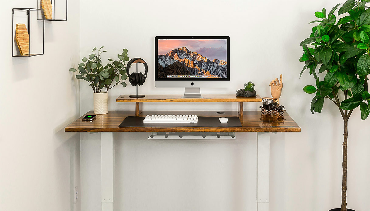 Scrivania ergonomica minimal con computer, cuffie e piante decorative.