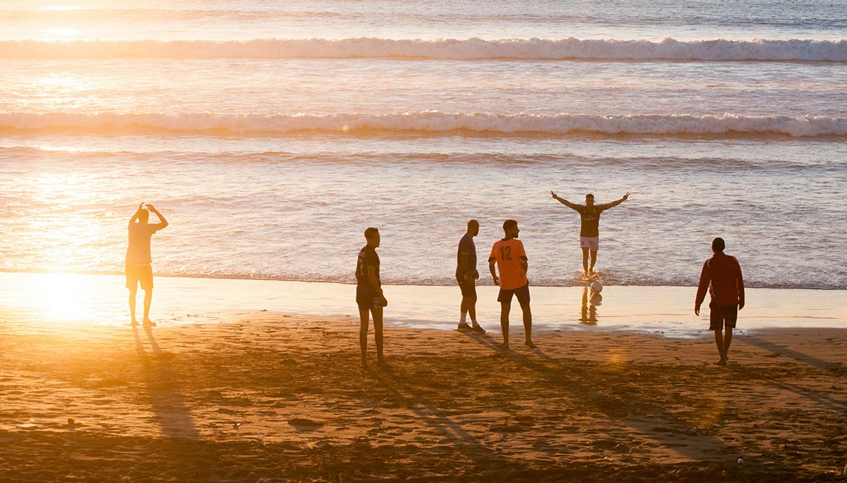 Persone che camminano in riva al mare al tramonto, immagine evocativa dei ricordi di viaggio