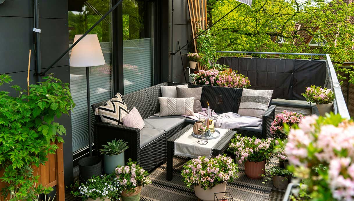 Terrazzo moderno con divano e piante in vaso, arredato con fiori rosa e verde