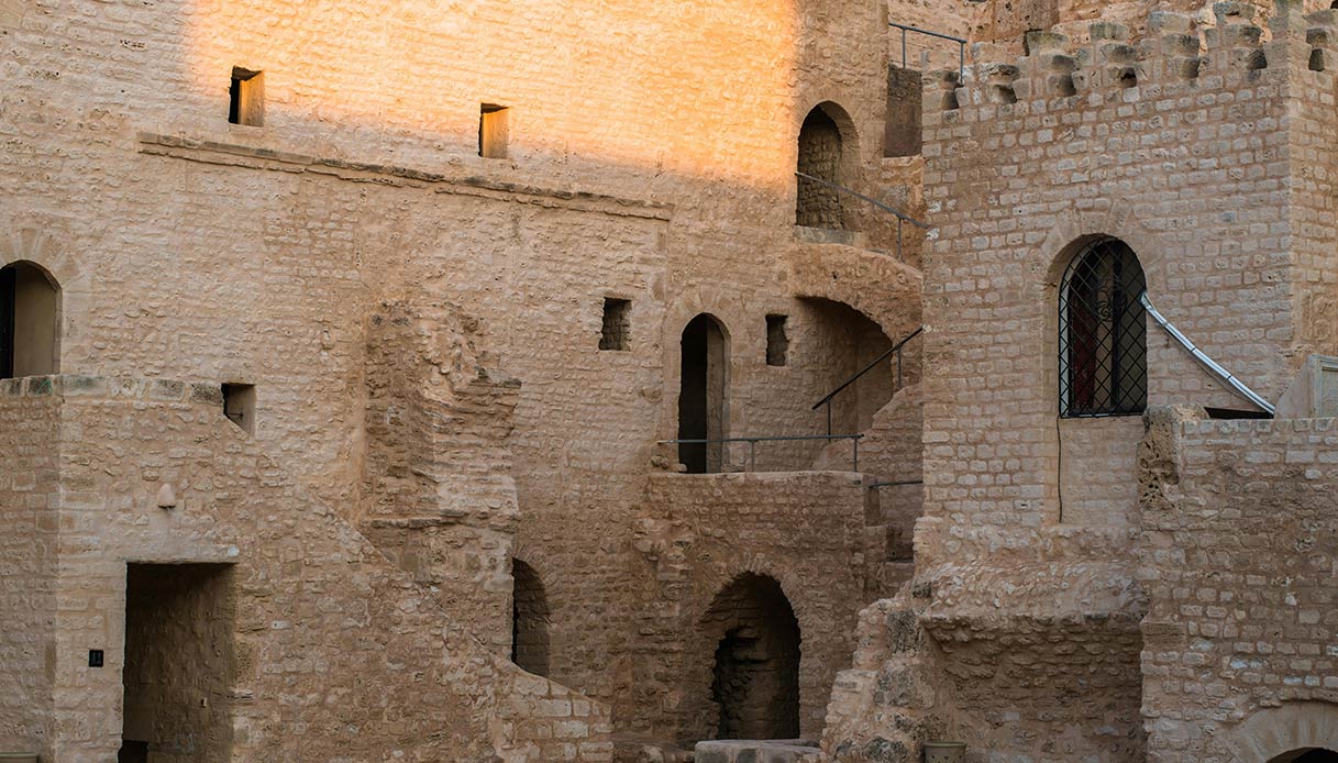 Dettaglio di mura e camminamenti in pietra di un castello medievale italiano illuminato dalla luce del tramonto