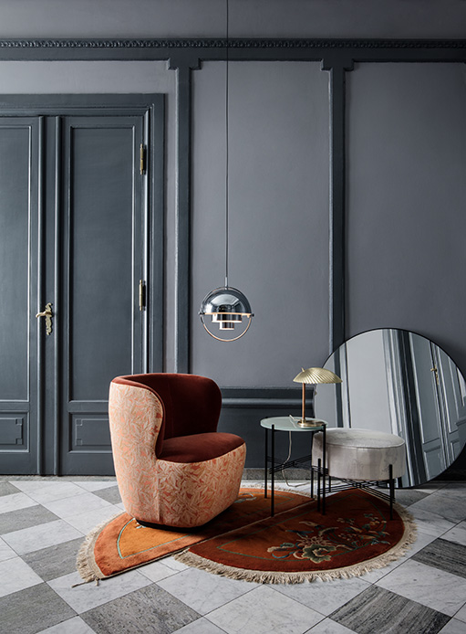 Soggiorno elegante con poltrona bordeaux e rosa, tappeto circolare e lampade metalliche sospese