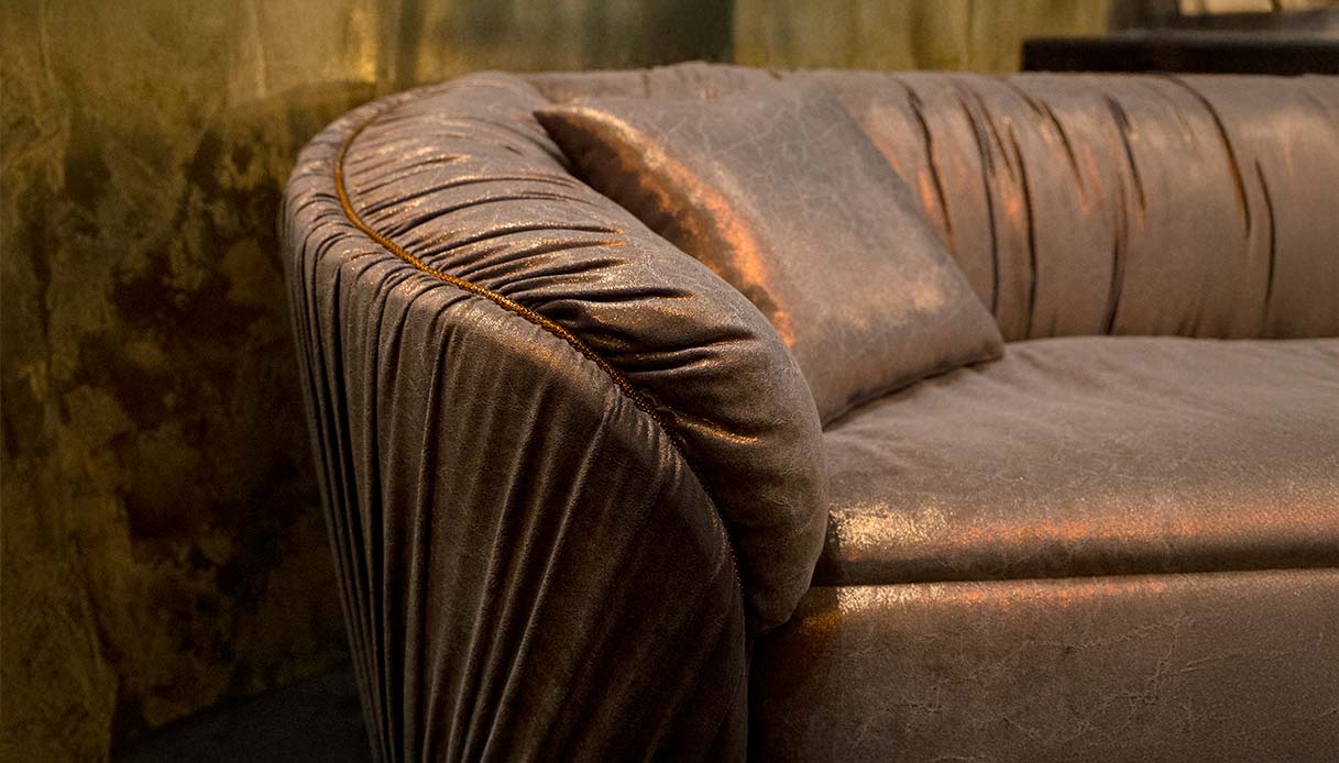 Dettaglio di un divano in velluto drappeggiato con riflessi dorati, ispirazione glamour per il living