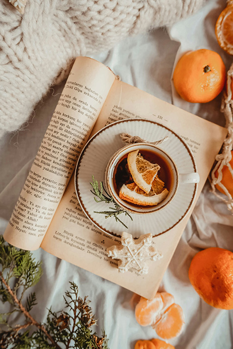 Tisana con agrumi su un libro aperto, accanto a clementine e maglia intrecciata