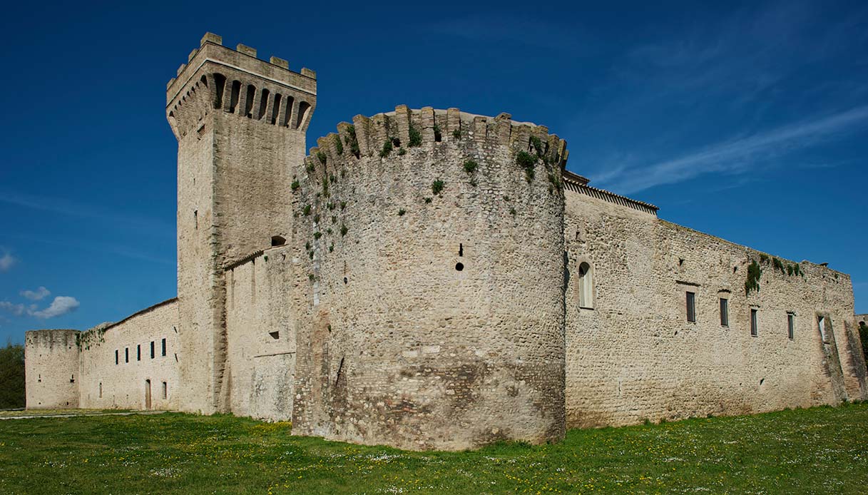 Veduta esterna della Torre della Botonta in Umbria, fortezza medievale con mura in pietra e torre merlata sotto un cielo azzurro