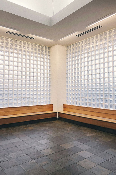 Pareti luminose in vetrocemento con panche in legno e pavimento in pietra