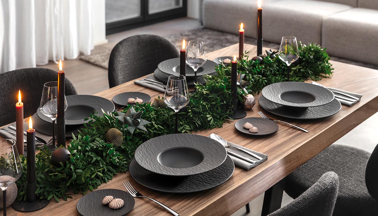 Tavola natalizia con piatti neri Manufacture Rock, candele scure e centrotavola verde in stile black Christmas.