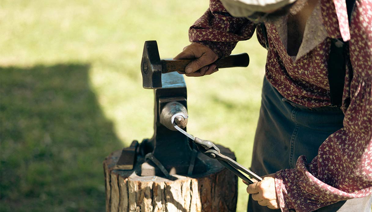 Primo piano di mani che lavorano il metallo con martello e incudine