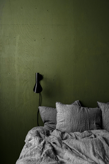 Letto in tessuti naturali su parete verde invecchiato dalle tonalità intense