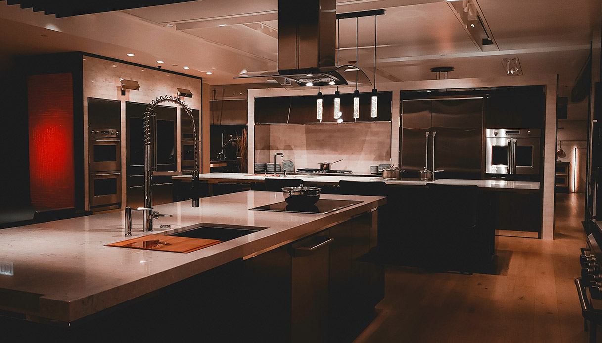 Cucina contemporanea con isola centrale, piani chiari e accenti metallici.