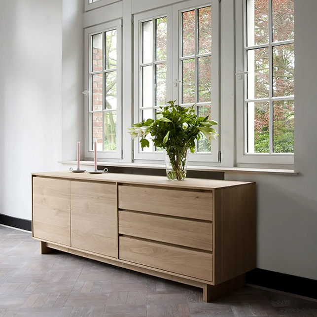 Credenza in legno naturale sotto grandi finestre con vaso di fiori
