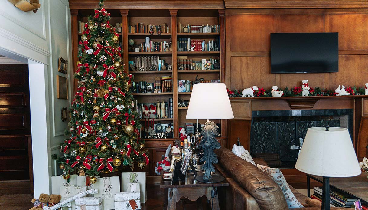 Soggiorno con albero di Natale tradizionale decorato in rosso e oro accanto a libreria in legno.