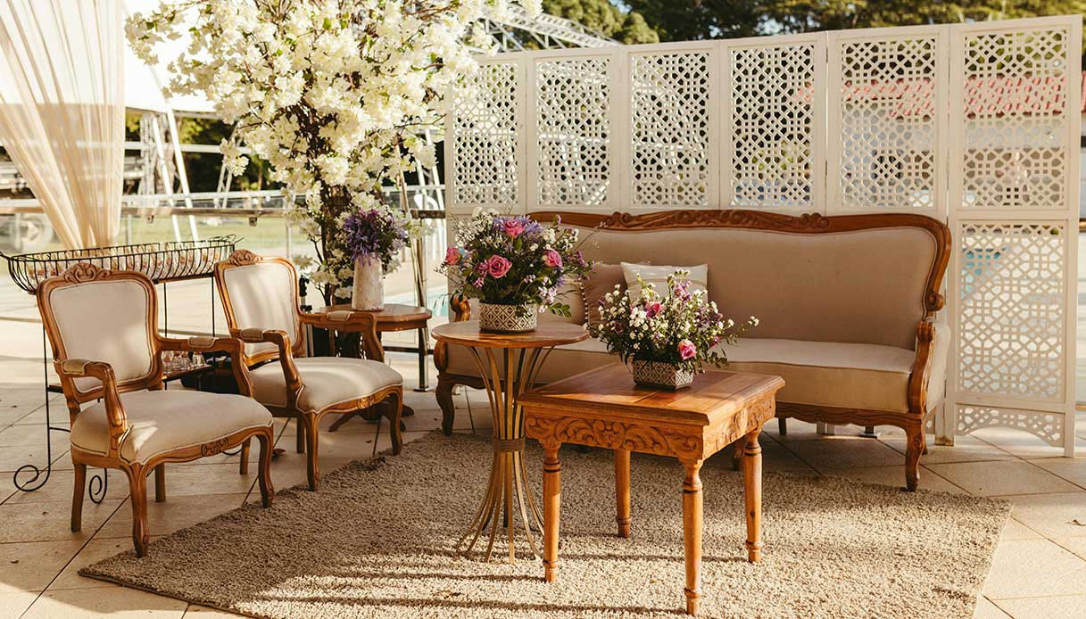Zona outdoor con tappeto materico e arredi classici in legno e tessuto chiaro.