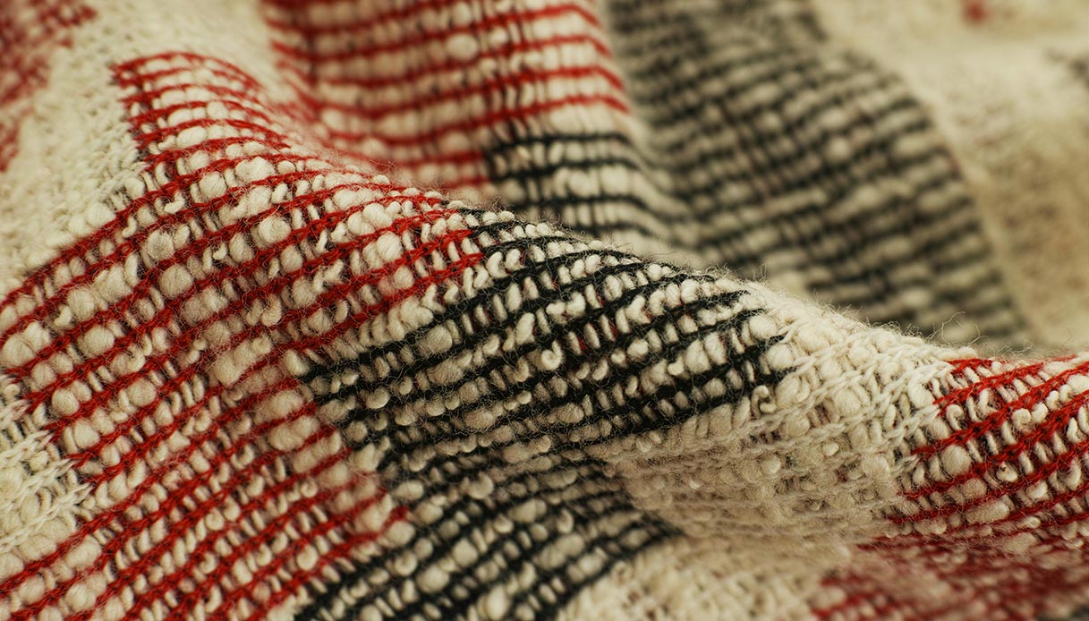 Dettaglio della tessitura di un tappeto in lana con fili rossi e neri.